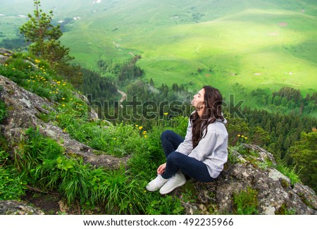 Beautiful woman sitting on mountain top and contemplating landscape