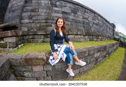 
A Beautiful Woman Is Sitting On The Neatly Arranged Rocks At Noon. This Photo Was Taken Using A Fish Eye Lens So The Image Looks Convex