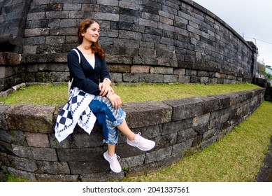 
A Beautiful Woman Is Sitting On The Neatly Arranged Rocks At Noon. This Photo Was Taken Using A Fish Eye Lens So The Image Looks Convex