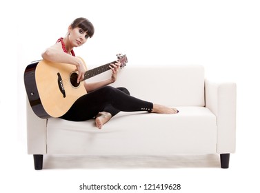 Beautiful Woman Sitting On The Sofa And Playing Guitar, Isolated On White