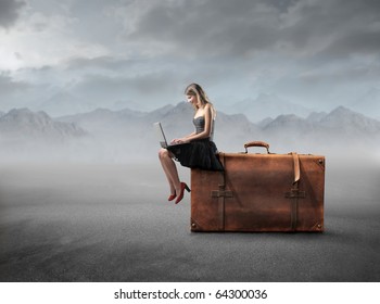 Beautiful woman sitting on a suitcase and using a laptop - Powered by Shutterstock