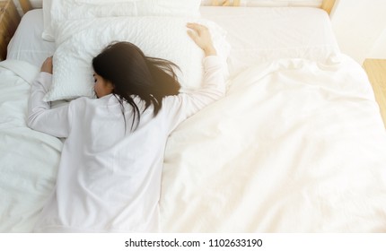 Beautiful woman sleeping in the bedroom.
Lady lying face down on the bed.Girl wearing a pajama sleep on a bed in a white room in the morning.Warm tone.
