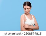 Beautiful woman with smear of body cream on her arm against light blue background, space for text