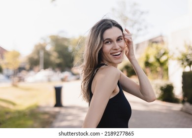 Beautiful Woman Smiling And Look At Camera In Countryside. Outdoor Portrait Of A Smiling Blonde Girl. Happy Cheerful Girl Laughing At Green City, Look Fashion And Show Toothy Smile. She Turn Around.