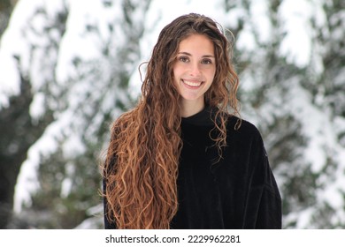 beautiful woman smiling and looking at camera on a snowy day. Long and curly hair. Snowy landscape. Forest on a cold winter day. Portrait of a Caucasian woman enjoying the snow. - Powered by Shutterstock