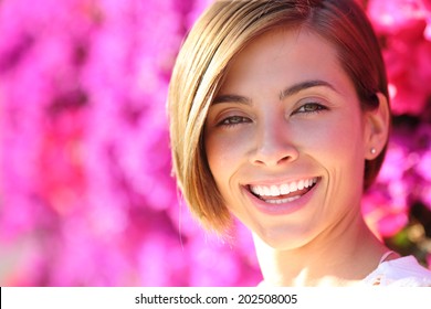 Beautiful woman smiling with white perfect teeth with a warmth lot of pink flowers in the background            