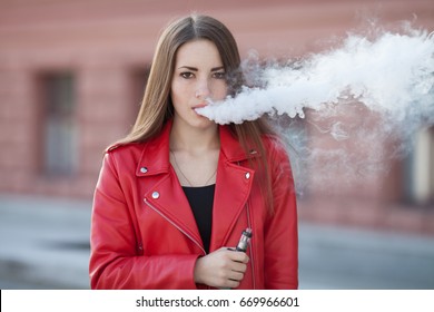 beautiful woman smoking ( vaping ) e-cigarette with smoke outdoors. Vaping concept.
