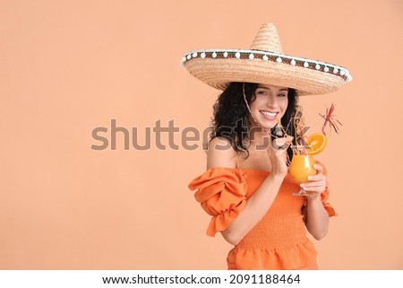 Beautiful woman in sombrero hat with orange juice on color background