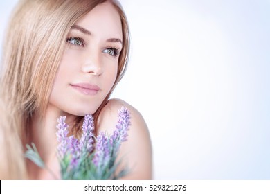 Beautiful woman at spa, closeup portrait of a nice blond girl enjoying aroma of a lavender flowers over clear background, using natural cosmetics, healthy lifestyle