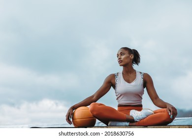 Beautiful woman in sports clothing sitting with medicine ball outdoors. Sportswoman relaxing after exercising on building terrace. - Powered by Shutterstock
