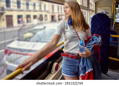 Beautiful woman is standing near window in the public transport. Young white pensive girl 20 years old in trolleybus.