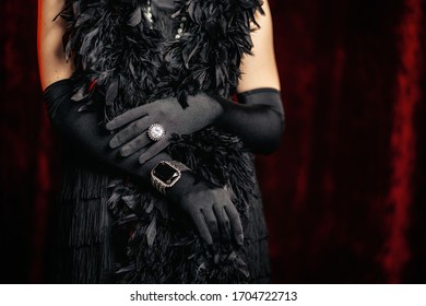 Beautiful woman standing in old historical 20th century in flapper dress with fringe, feathers boa on red background. Details of Gatsby costume, treasure jewelry.