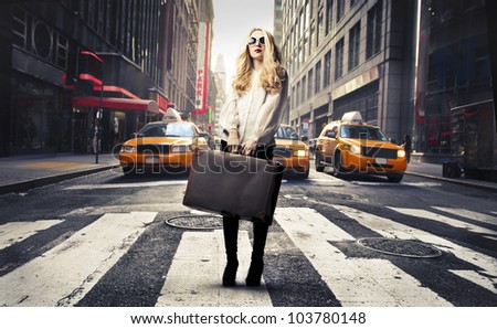 Beautiful woman standing on a crosswalk and holding a suitcase