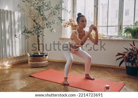 Beautiful woman standing in squatting position while practicing in front of the window at home