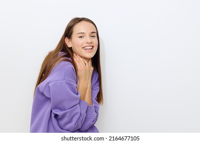 a beautiful woman stands on a white background in a purple tracksuit joyfully presses her hands to her neck, slightly hunched over