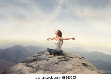 Beautiful woman stretching out her arms while sitting on a peak over the mountains