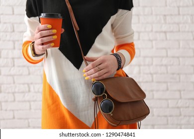 Beautiful woman with stylish accessories and cup of coffee on white brick background
