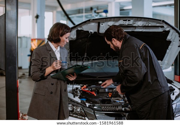 Beautiful a woman in a suit and in service auto have\
a conversation with the mechanic over the car he shows the problem\
of the car