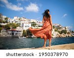 Beautiful woman in summer dress stands on the rock and looks at the city of Skiathos