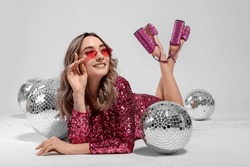 Beautiful Woman In Sunglasses And Sequin Dress Among Disco Balls On White Background