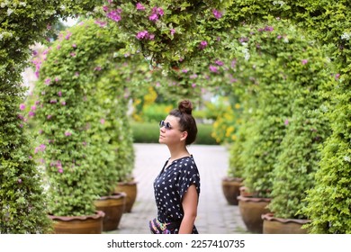 Beautiful woman in sunglasses stands under arches covered in flowers - Shutterstock ID 2257410735