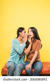 a beautiful woman is surprised when her friend whispers while chatting sitting together on the couch