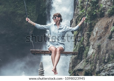 Beautiful woman swings near waterfall in the jungle of Bali island, Indonesia.
