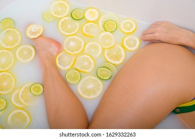 Beautiful Woman Takes A Milk Bath With Lemon And Lime Slices. Skin Care And Whitening. A Girl In A Yellow-green Bikini Does The Cleopatra Rejuvenation Procedure.