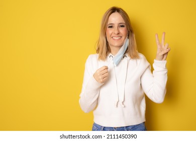 Beautiful Woman Taking Her Surgeon Mask Off Isolated Over Yellow Studio Background.