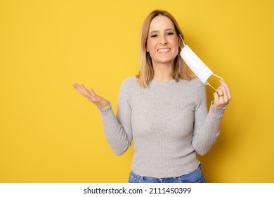 Beautiful Woman Taking Her Surgeon Mask Off Isolated Over Yellow Studio Background.