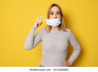 Beautiful Woman Taking Her Surgeon Mask Off Isolated Over Yellow Studio Background.