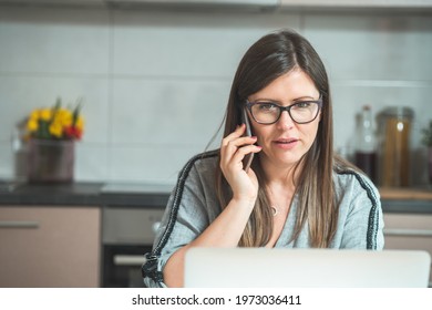 Beautiful Woman Talking On The Phone And Working At Home On Laptop Computer
Serious Businesswoman Sitting At Desk And Looking In Laptop Computer While Speaking With Coworkers Or Clients On Smartphone.