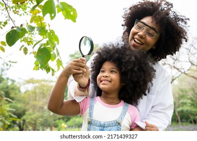 Beautiful Woman Teaching Young Kid Examining Green Leaf Through A Magnifying Glass In The Garden. Concept Of Self Learning In Springtime.