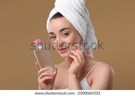 Beautiful woman in terry towel removing makeup with cotton pad on beige background