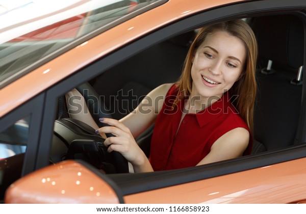Beautiful woman\
testing and choosing new comfortable car before buying in auto\
showroom. Attractive redhaired lady sitting in automobile, driving\
and looking at rear view\
mirror.