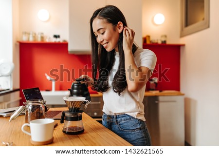 Beautiful woman touches her hair and with smile makes coffee in kitchen