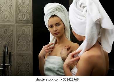 Schöne Frau im Handtuch, die den Spiegel anschaut.