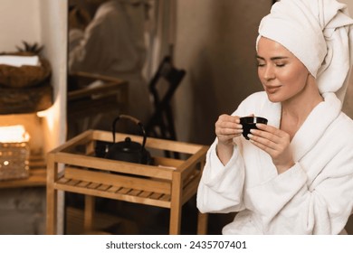 Beautiful woman with towel on her head drinking herbal tea after spa procedures. Wellness spa - Powered by Shutterstock