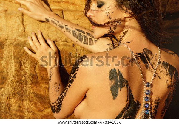 Beautiful woman with trace of car tire on her body\
is posing beside the sand\
cliffs