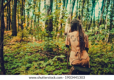 Beautiful woman in traditional tribal dress meditating in the woods, native american indian shaman meditating outdoors, natural medicine concept