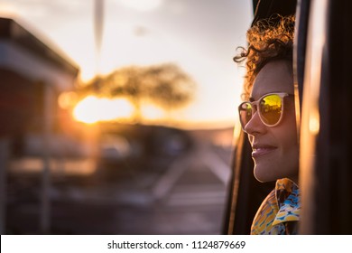 Beautiful Woman Travel On A Car Looking Outside And Enjoy The Light Of The Golden Sunset On Her Face. Nice Lifestyle And Peaceful Emotions Traveling Around The World