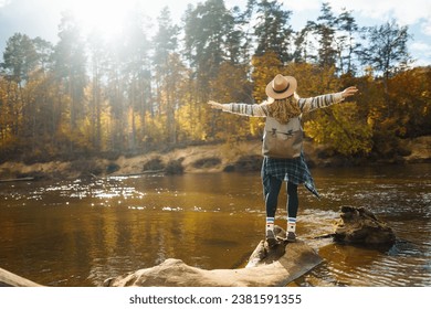 Beautiful woman traveler enjoying autumn hiking along the river. A traveler walks in the autumn forest, enjoying the weather. Active lifestyle. - Powered by Shutterstock