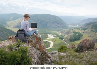 Schöne Frau Reisenden in einem Hut in den Bergen mit einem Laptop. Arbeiten Sie außerhalb des Büros.