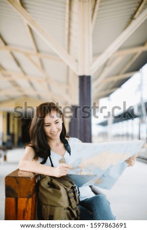 Beautiful woman traveler holding location map in hands and sitting at train station