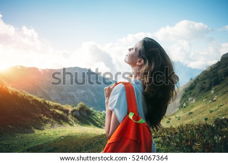 Beautiful woman traveling in mountain meadows. With small backpack and long weaving hair. Evening with sunset