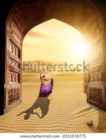 Beautiful woman in Tribal costume dancing on the sand near the ancient arch at sunset and caravan background in Rajasthan, India