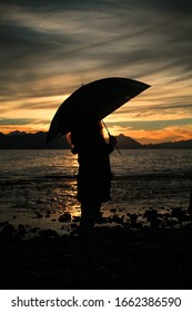 

beautiful woman with an umbrella on the sea coast with sunset background

