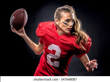 Beautiful woman in uniform playing american football with ball isolated on black