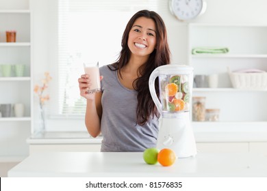 Beautiful woman using a blender while holding a drink in the kitchen - Powered by Shutterstock