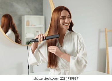 Mujer hermosa usando plancha de pelo en la habitación